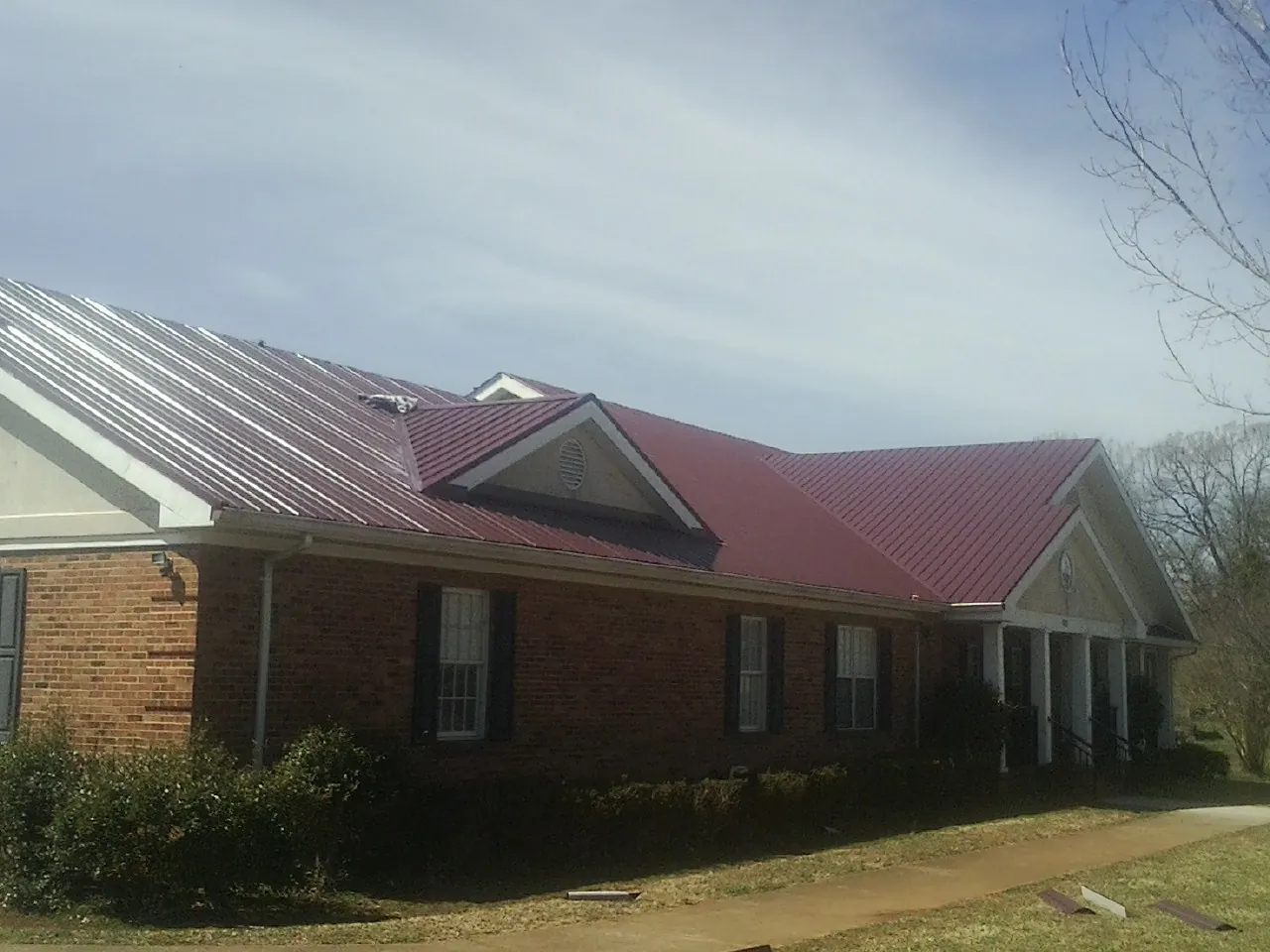 Red metal roof with gabled entries on a long brick building, from a Hail Damage Roof Repair job in Syracuse